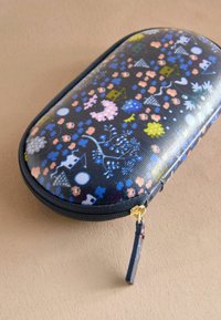 Črna zadrgasta torbica s pisanimi cvetličnimi in hišnimi motivi ter sijočo površino in zlato zadrgo. Kompaktna, ovalna oblika.