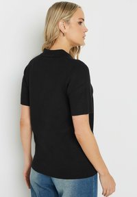 Svart kortärmad polo med krage, slät textur och luftig passform. Designen inkluderar en söm i ryggen för form.