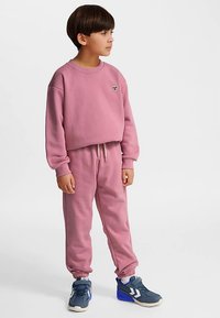 Lyserødt svedsæt med cropped sweatshirt med lille logo og matchende joggers med elastiske manchetter, kombineret med blå atletiske sko.