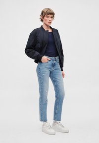 Tamsiai mėlyna bombonešio striukė, aptempta juoda palaidinė, šviesiai mėlyni suplėšyti džinsai ir balti sportbačiai. Lygus audinys, laisvas siluetas ir kasdienis stilius.