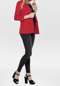 Blazer rojo con un diseño entallado, combinado con una blusa negra, jeans skinny negros y sandalias de plataforma negras con tiras al tobillo.