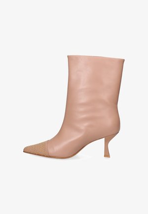 Botte en cuir beige mi-mollet avec un bout pointu orné de clous dorés et un talon aiguille fin et courbé.