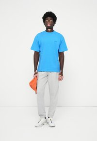 Blå bomulds t-shirt, kortærmet, afslappet pasform. Grå sweatpants med blød tekstur. Orange kasket i hånden. Hvide sportssko med farveaccenter.