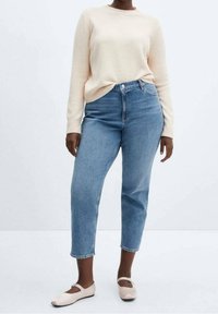 Suéter de punto beige claro, jeans azules de cintura alta y zapatos planos claros. El suéter tiene un cuello redondo, mientras que los jeans tienen un corte relajado y piernas recortadas.