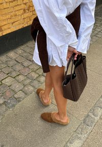 Bordeaux umetni krzneni obložen klompe, krema pulover obleka, temno rjava tkanina torba. Kameniti poti z kamnito teksturo, topla osvetlitev.