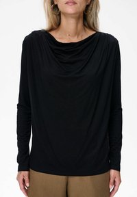 Zwarte lange mouw top met een gedrapeerde cowl halslijn, gemaakt van zachte stof; gecombineerd met tan broek, met een strakke ontwerpen en minimale details.