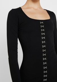 Černý body s dlouhým rukávem a čtvercovým výstřihem, s centrálním řadou stříbrných patentek, vyrobený z měkkého a elastického materiálu.