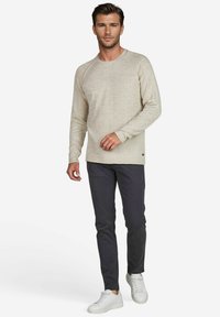 Hellbeige strukturierter Pullover mit Rundhalsausschnitt und langen Ärmeln, kombiniert mit dunklen Slim-Fit-Hosen und weißen Sneakers.