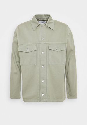 Veste-chemise vert clair avec col pointu et deux poches poitrine à rabat, présentée sur un fond blanc uni.