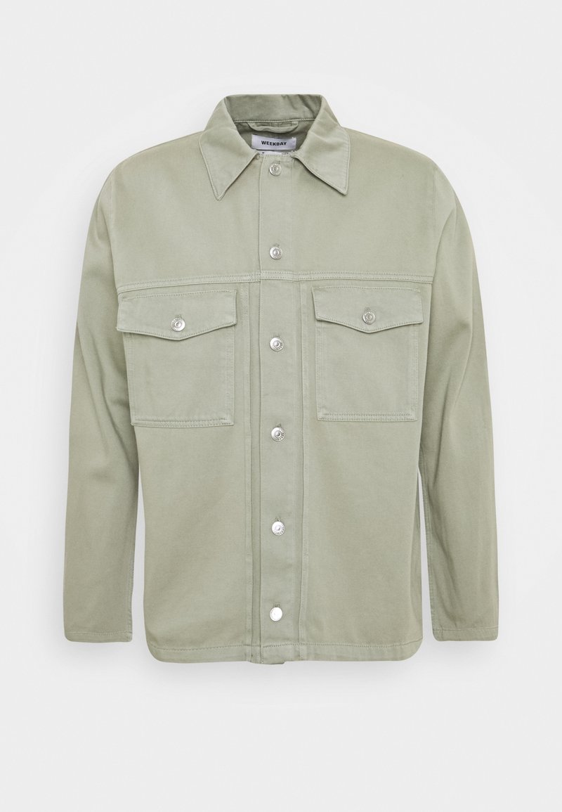 Veste-chemise vert clair avec col pointu et deux poches poitrine à rabat, présentée sur un fond blanc uni.