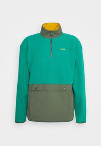 Pullover in pile di colore teal con collare giallo, zip frontale e pannello inferiore verde dotato di tasca a pouch. Tessuto strutturato con accenti a contrasto.
