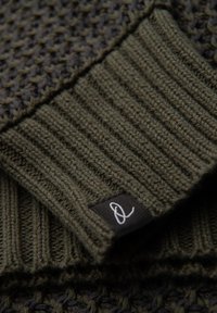 Suéter de punto en verde oliva oscuro, con patrones texturizados y un dobladillo acanalado. Se adjunta una pequeña etiqueta negra con un logo blanco.