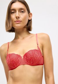 Κόκκινο σουτιέν δαντέλας με λουλουδάτα σχέδια, ημιδιαφανή cups και ρυθμιζόμενα λουράκια με μεταλλικές λεπτομέρειες. Λεια πανωλεθρία για άνεση.