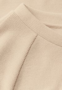 Tessuto beige a righe con una superficie texturizzata, caratterizzato da un colletto arrotondato. Il materiale è morbido e presenta un motivo distintivo e sottile.