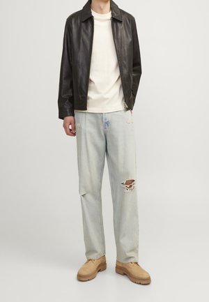 Chaqueta de cuero negra, camiseta crema, jeans rasgados de color azul claro y botas beige. La chaqueta tiene un cuello y cierre de cremallera. Estilo urbano casual.