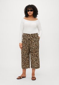 Pantaloni culotte con stampa leopardata e cintura elastica, abbinati a una maglietta a maniche lunghe bianca. Il modello indossa occhiali da sole neri e sandali marroni.