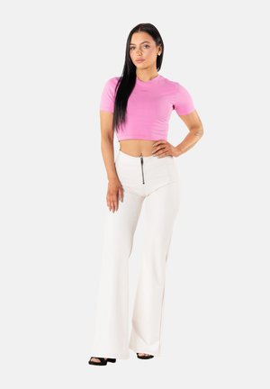 Camiseta rosa corta y pantalones anchos blancos con cierre frontal. El conjunto presenta una textura suave y una silueta ajustada. Sandalias negras de tacón.