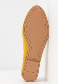 Chaussure plate en daim jaune montrant une semelle extérieure en caoutchouc brun texturé avec le logo ALDO, bout pointu et petit talon carré sur fond blanc.