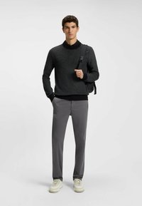 Dark gray knit sweater with a textured weave and ribbed cuffs, paired with light gray trousers and white sneakers, featuring a shoulder bag.