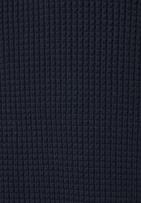 Marineblauer Strickstoff mit gerippter Textur, gekennzeichnet durch gleichmäßig verteilte vertikale Linien und ein weiches, dickes Aussehen.