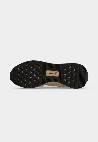 Semelle d'une chaussure Polo beige avec une semelle en caoutchouc noir arborant des motifs hexagonaux et un logo Polo rectangulaire au centre.