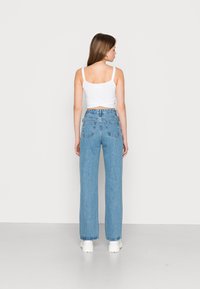 Top cropped branco com alças finas, combinado com jeans de perna larga, de cintura alta, em azul claro. Os jeans possuem bolsos traseiros e uma textura ligeiramente desbotada.
