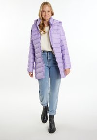 Giacca a vento viola con cappuccio, caratterizzata da una chiusura zip frontale, polsini a costine e un design a righe verticali. Indossata sopra un maglione crema e jeans blu.