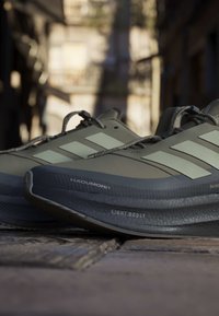 Paar graue Adidas-Laufschuhe mit leichten Boost-Sohlen auf einer Kopfsteinpflasterstraße im sanften Sonnenlicht.