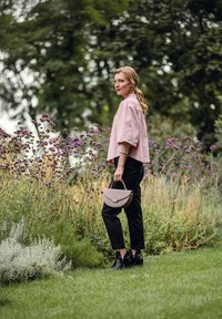 Světle růžový zkrácený top s nabíranými rukávy, černé úzké kalhoty a levandulová kabelka. Scéna zahrnuje zelené listí a fialové květiny.