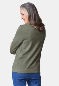 Khaki groene trui met lange mouwen en ronde hals. Zachte textuur en eenvoudig design, gecombineerd met blauwe spijkerbroek.