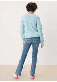 Pull bleu clair en maille avec manches à boucles texturées, associé à un jean évasé bleu délavé et des baskets blanches avec des accents roses.