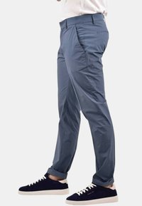 Chinos azzurro chiaro con una superficie liscia e tasche frontali, indossati con sneakers blu navy con dettagli bianchi e un profilo basso.