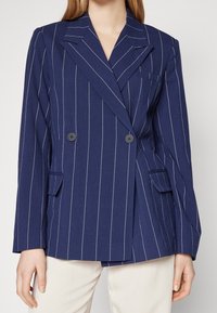 Marlová navy modrá dvouřadá sako s bílými pruhy, klopami, dvěma knoflíky a předními kapsami, vyrobené z texturované látky.