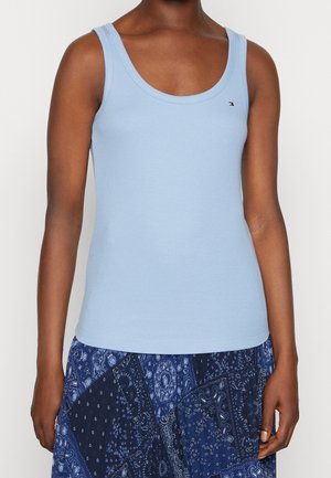 Persoon draagt een lichtblauw mouwloos hemd en een blauwe rok met een paisley-patroon.