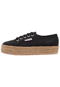 Zapatilla de lona negra con suela de plataforma gruesa de yute trenzado. Cuenta con cinco ojales metálicos y una pequeña etiqueta de logo en el lateral.