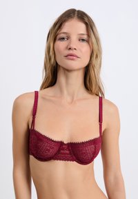 Burgundzka koronkowa biustonosz z drucikami, ozdobiony delikatnymi floralnymi wzorami, z regulowanymi ramiączkami i falbaniastym wykończeniem.