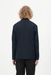 Tume sinine nööpidega särk, millel on pikad varrukad, krae ja sile tekstuur. Tagantvaade näitab sirget lõiget ja minimalistlikku disaini.