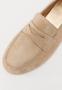 Beige semsket slip-on loafer med sømdetaljer og en subtil frontprofil. Glatt tekstur med rund tå og lavprofildesign.