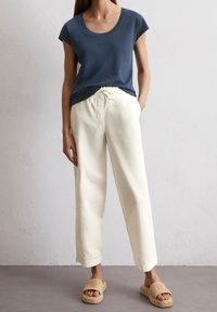 Marinblå t-shirt med kort ärm i kombination med krämfärgade lösa byxor med dragsko i midjan och sandfärgade, texturerade slide-sandaler.