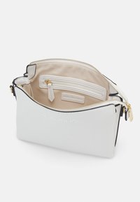 Bílo-kůže taška s zipovým uzávěrem, s b éžovým látkovým interiérem, vnitřní kapsou na zip a embosovaným logem na vnější straně.