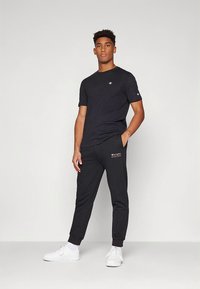 Musta puuvillainen t-paita ja siihen sopivat collegehousut. Paidassa on pieni logo rinnassa ja sivulla, sekä resorit hihansuissa. Valkoiset lenkkarit täydentävät asun.