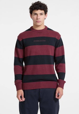 Bordeaux en marine gestreepte trui met geribbelde manchetten en halslijn. Heeft het logo "GUESS JEANS" in contrasterende kleur op de borst.
