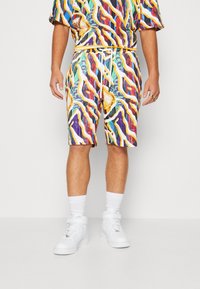 Chemise à manches courtes et shorts mi-genou dans un motif abstrait multicolore vibrant, en tissu léger, assortis à des baskets blanches.