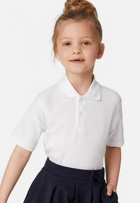 Hvid polo med blød tekstur og tre knapper, kombineret med en mørk marineblå nederdel med sløjfedetalje ved taljen.