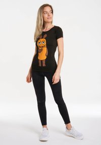 Black short-sleeve t-shirt featuring a cartoon character with orange and brown accents. Paired with dark jeans and white sneakers.
