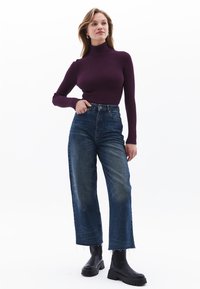 Burgundy ribbad polokrage-sweater kombinerad med högmidjade, vida blåjeans och svarta ankelstövlar med en kraftig sula.