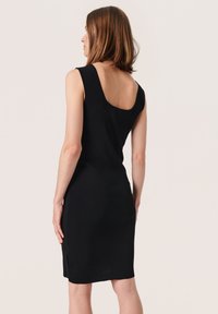 Robe sans manches noire avec un dos rond, forme ajustée, texture côtelée et coupe à mi-genoux, mettant en valeur une silhouette simple et élégante.