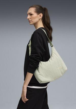 Borsa a spalla verde chiaro con una consistenza morbida e gonfia e cuciture in tonalità simile. Tracolla regolabile. Felpa nera indossata con pantaloni scuri.