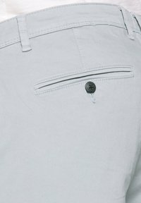 Hellgraue Baumwollhose mit einer Gesäßtasche, die einen schwarzen Knopf und Nahtdetails entlang des Bunds und der Tasche aufweist.