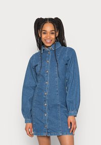 Vestido de camisa em denim azul médio, com mangas bufantes longas, frente com botão, colarinho e fendas laterais na bainha.
